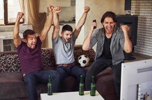 es ist ein Ziel. aufgeregt drei freunde, die zu hause gemeinsam fußball im fernsehen gucken foto