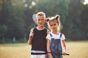 Porträt von Jungen und Mädchen, die an sonnigen Tagen mit Tennisschlägern in den Händen auf dem Feld stehen foto