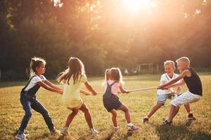 Kinder, die an sonnigen Tagen auf der schönen Wiese Tauziehen spielen foto