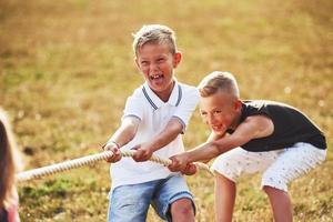 Kinder, die an sonnigen Tagen auf der schönen Wiese Tauziehen spielen foto