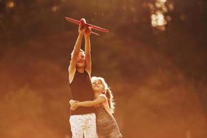 Mädchen und Jungen haben Spaß im Freien mit rotem Spielzeugflugzeug in den Händen foto