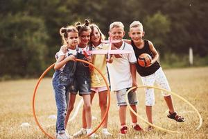 junge kinder mit fußball, flugzeugspielzeug und fitnesskreisen stehen an sonnigen tag zusammen auf dem feld foto