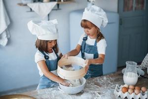 gebrauchtes Sieb. Familienkinder in weißer Kochuniform bereiten Essen in der Küche zu foto