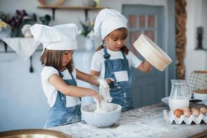 gebrauchtes Sieb. Familienkinder in weißer Kochuniform bereiten Essen in der Küche zu foto