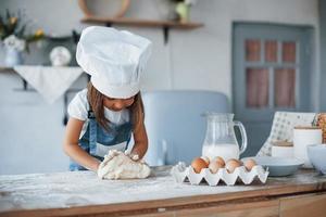 süßes kind in weißer kochuniform, das essen in der küche zubereitet foto