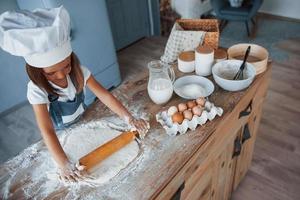 süßes kind in weißer kochuniform, das essen in der küche zubereitet foto