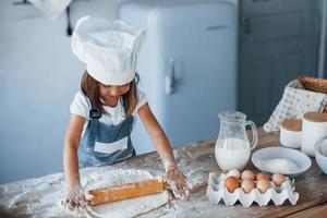 süßes kind in weißer kochuniform, das essen in der küche zubereitet foto