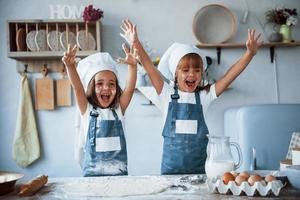 viel Spaß während des Prozesses. Familienkinder in weißer Kochuniform bereiten Essen in der Küche zu foto