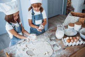 Konzentration aufs Kochen. Familienkinder in weißer Kochuniform bereiten Essen in der Küche zu foto