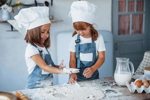 Konzentration aufs Kochen. Familienkinder in weißer Kochuniform bereiten Essen in der Küche zu foto