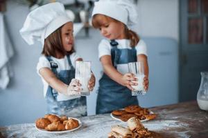 mit Gläsern mit Milch. Familienkinder in weißer Kochuniform bereiten Essen in der Küche zu foto