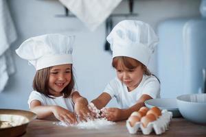 Konzentration aufs Kochen. Familienkinder in weißer Kochuniform bereiten Essen in der Küche zu foto