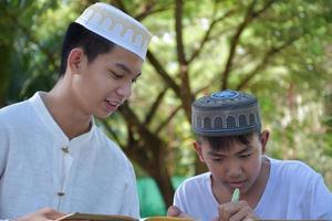 asiatische muslimische jungen sitzen im schulpark zusammen, um zu lesen und ihre täglichen aktivitäten zu lernen und in ihrer freizeit hausaufgaben zu machen, bevor sie nach hause zurückkehren, weicher und selektiver fokus. foto