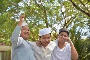 junge asiatische muslimische jungen hoben die hände, lächelten und umarmten sich, um glück unter den bäumen im park zu präsentieren, weicher und selektiver fokus. foto