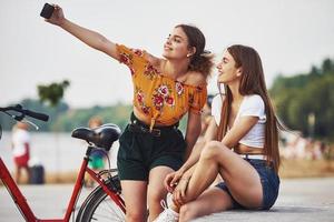 ein Selfie machen. Zwei junge Frauen mit Fahrrad amüsieren sich im Park foto