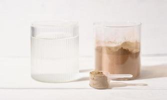 Molkenproteinpulver mit Schokoladengeschmack in einem Löffel neben einem Glas Wasser. Wellnessprodukt für Gewichtszunahme, Energieunterstützung und gesundes Leben. foto