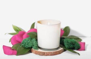 brennende Duftkerze aus weißem Glas mit Dekor aus Rosenblättern und grünen Blättern. Stilvolle Hausdekoration, Details eines gemütlichen Zuhauses