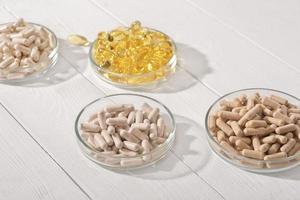 Nahrungsergänzungsmittel in Kapseln in Petrischalen auf weißem Holztisch. Omega 3 und verschiedene Vitaminpillen zur Unterstützung des Herz- und Gefäßsystems. foto
