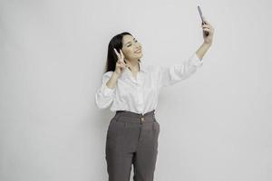 ein Porträt einer glücklichen asiatischen Frau, die ein weißes Hemd trägt und ihr Telefon hält, isoliert durch weißen Hintergrund foto