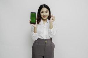 eine glückliche junge asiatische frau, die ein weißes hemd trägt und formherzgesten zeigt, drückt zärtliche gefühle aus, während sie kopienraum auf ihrem telefon zeigt foto