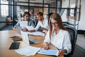 Blondes Mädchen liest Dokument. junge geschäftsleute in formeller kleidung, die im büro arbeiten foto