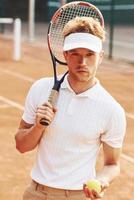 hält Ball in der Hand. junger tennisspieler in sportlicher kleidung ist draußen auf dem platz foto