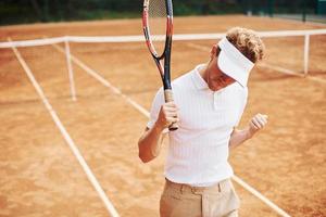 Sieg feiern. junger tennisspieler in sportlicher kleidung ist draußen auf dem platz foto