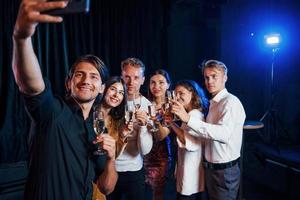 macht ein Selfie. gruppe fröhlicher freunde, die drinnen mit getränken in den händen neujahr feiern foto