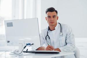 Der junge stilvolle männliche Arzt mit Stethoskop ist tagsüber in der Klinik foto