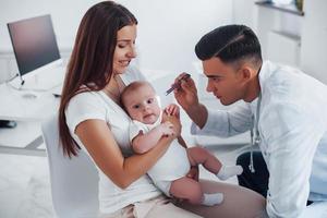 mit Mutters Hilfe. Junge Kinderärztin ist tagsüber mit kleinem Baby in der Klinik foto