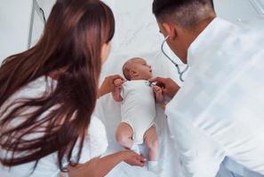 Zuhören mit Stethoskop. Junge Kinderärztin ist tagsüber mit kleinem Baby in der Klinik foto