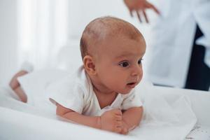 kleines baby, das auf dem tisch liegt. Junge Kinderärztin ist tagsüber in der Klinik foto