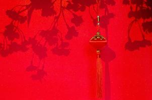 hängender anhänger für chinesische neujahrsverzierung mit schatten von pfirsichblütenblumen auf rotem glitzerpapierhintergrund. foto