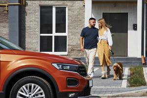 einander umarmen. Schönes Paar macht einen Spaziergang zusammen mit Hund im Freien in der Nähe des Autos foto