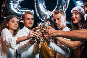 Brille klopfen. gruppe fröhlicher freunde, die drinnen mit getränken in den händen neujahr feiern foto