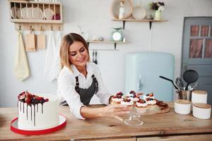 positive Blondine mit ihren hausgemachten leckeren Keksen und Kuchen in der Küche foto