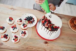 Nahaufnahme einer Frau, die Sahne auf den Kuchen in der Küche gießt foto