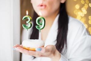 frau, die einen kuchen mit den kerzen der nummer 39 auf festlichem unscharfem bokeh-hintergrund hält foto