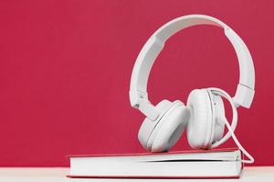 Hörbuchkonzept mit Kopfhörern und einem Buch auf viva magentafarbenem Hintergrund. ein Buch hören. foto