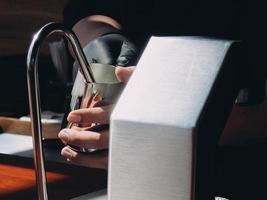 barista in schürze hält kaffeemaschine aus aluminiummetall. auf Holztisch foto