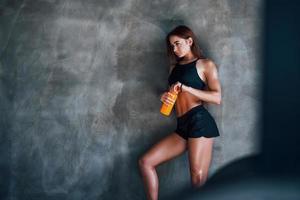 mit Flasche Wasser. junge fitnessfrau mit schlankem körper und in schwarzer sportlicher kleidung ist im fitnessstudio foto