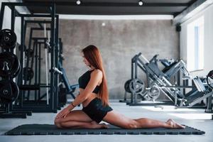 junge Frau mit schlankem Körperbau und in schwarzer sportlicher Kleidung beim Yoga auf der Fitnessmatte foto