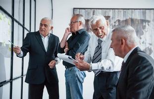 Arbeiten mit Aufklebern auf Glas. Ein älteres Team älterer Geschäftsmannarchitekten trifft sich im Büro foto