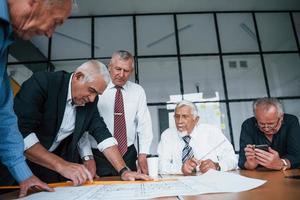 Bauplanung durch Aufmaß auf Papier. Ein älteres Team älterer Geschäftsmannarchitekten trifft sich im Büro foto