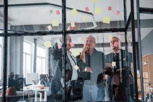 funktioniert mit Aufklebern auf dem Glas. Ein älteres Team älterer Geschäftsmannarchitekten trifft sich im Büro foto