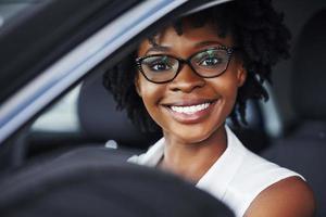 glückliches Lächeln. junge afroamerikanische frau sitzt im neuen modernen auto foto