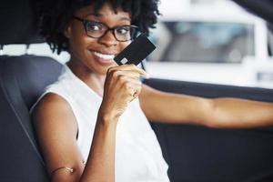 Kreditkarte besitzt. junge afroamerikanische frau sitzt im neuen modernen auto foto