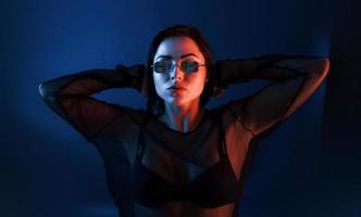 heiße brünette mit sonnenbrille posiert im studio mit neonbeleuchtung foto