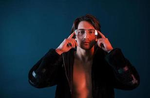 schöner langhaariger heißer mann mit brille ist im studio mit blauer neonbeleuchtung foto