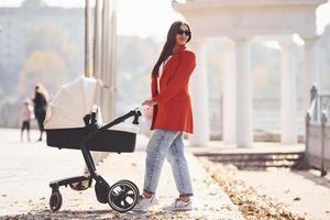 mutter im roten mantel geht zur herbstzeit mit ihrem kind im kinderwagen im park spazieren foto